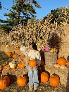 a woman sitting on hay bales with pumpkins