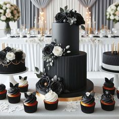 a black and white wedding cake surrounded by cupcakes on a table with flowers