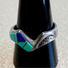 a silver ring with blue and green stones on it's side sitting on top of a black object