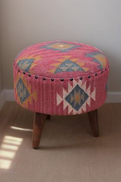 a pink ottoman sitting on top of a wooden floor next to a wall and window