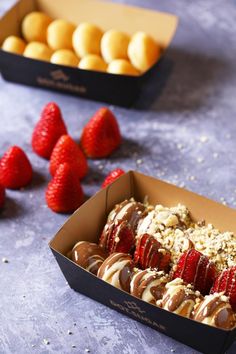 two boxes filled with strawberries and chocolate covered pastries next to some other desserts