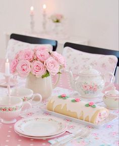 the table is set with pink roses and teacups, plates, cups, and candles