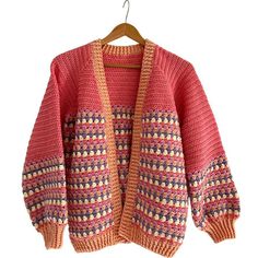 a pink and orange sweater hanging on a clothes hanger with an open knitted cardigan