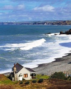 a small house sitting on top of a lush green hillside next to the ocean with waves coming in