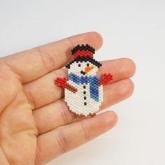 a hand holding a small beaded snowman brooch