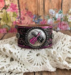 v'¯) .`*.¸.*' ★ LOve LoVe LovE this one! ★ ¸.*'.*'¨) ¸. (¸.*'(¸.*' (¸. This DESIGN ~ ❤ Silver double guitar was brought to life with hot pink and black patina and layered over a black filigree. ❤ Handpainted tooled leather in colors and pink and black, distressed and sealed. ❤ Width of leather is approximately 1 1/2 inches. BRACELET SIZING INFO: My women's bracelets are approximately 8 1/2 inches end to end. I place 2 snaps at 7 and 7 3/4 inches for adjustability. Jewelry for your heart & so Adjustable Concho Cuff Bracelet For Festival, Adjustable Punk Cuff Bracelet For Festival, Adjustable Rock Bracelets For Concerts, Adjustable Rock Style Bracelets For Concerts, Adjustable Music-themed Bracelets For Concerts, Adjustable Concho Cuff Bracelet Gift, Adjustable Music-themed Jewelry For Concerts, Adjustable Rock Style Leather Bracelet For Gift, Guitar Bracelet