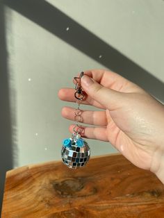 a person holding onto a disco ball shaped keychain on a wooden table in front of a window