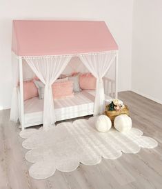 a white bed with pink canopy and pillows on the floor in front of a wall