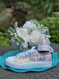 Hand Glittered unbranded canvas sneakers glittered in a gorgeous chunky white mix called *bungalow* with teal glitter personalization.  Made to order. Ivory glitter sneakers with teal personalization to include name on the outside of each sneaker and date down the back as shown. Please include custom info in the order notes. Should you desire different placement or options, please send us a message. Matching glittered trim also available (as shown in listing photos) in place of black strip.  See options at checkout. Check out our other white personalized wedding sneaker options here: https://www.etsy.com/shop/GlitterItGlam/edit?ref=edit_trust_header§ion_id=46070397 Glitter is high quality and heat set for minimal glitter loss and lasting quality, though, you may see glitter shedding the fi Low-top Glitter Sneakers For Wedding, Party White Sneakers With Glitter Accents, White Glitter Party Sneakers, White Low-top Sneakers With Glitter Print, Sneakers For Wedding, Bling Sneakers, Sparkle Sneakers, Bride Sneakers, Ivory Wedding Shoes