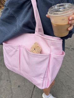 a person holding a pink bag with a teddy bear in it and a cup of coffee