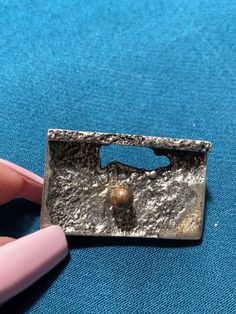 This unique piece of jewelry was created by the one and only Robert Larin. Robert Larin was a Canadian Montreal designer who was passionate about working with pewter and other metals. This piece is from the 1970s and has his first and last name stamped on the back to make it very special. This stunning square brooch is made out of pewter and brass. It has a very particular look to it. It has a variety of textures and dimensions in the front of the brooch. Not only that, it has a brass ball in th Unique Metal Brooch Gift, Metal Lapel Pin Brooch As Gift, Indian Fabric, Blanket Wrap, The One And Only, The 1970s, Pin Badges, One And Only, Making Out