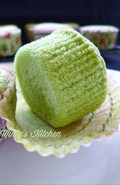 a green cake sitting on top of a white plate next to cupcakes in the background