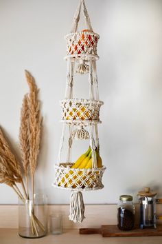 three tiered hanging fruit basket with bananas and straws in front of a white wall