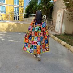 a woman is walking down the street wearing a colorful coat with flower designs on it