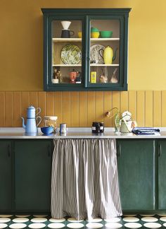 a kitchen with yellow walls and green cabinetry, striped table cloth on the counter