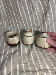 a hand is holding three small ceramic pots