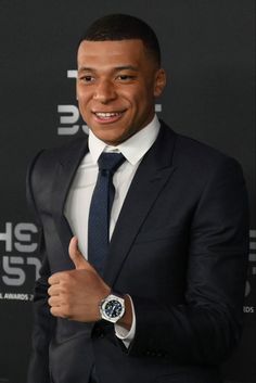 a man in a suit and tie giving the thumbs up sign with his hand while wearing a watch