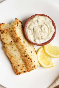 grilled fish with tartar sauce and lemon wedges on a white dinner plate