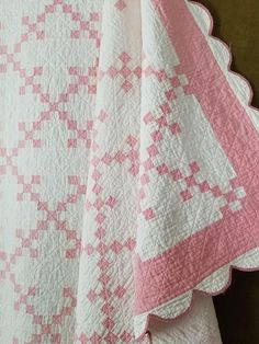 a pink and white quilt is hanging on a wall