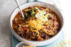 a bowl filled with chili and cheese on top of a blue place mat next to a spoon