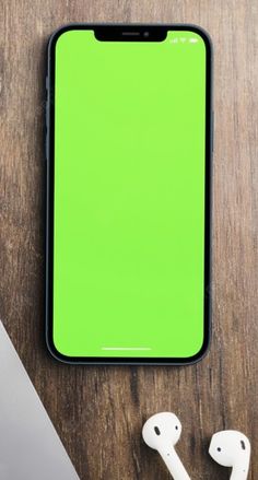 an iphone, headphones and laptop on a wooden table with a green screen in the background