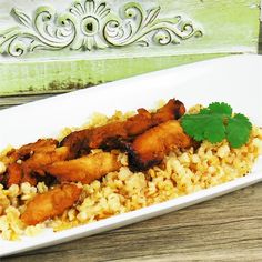 a white plate topped with rice and chicken next to a green leafy garnish