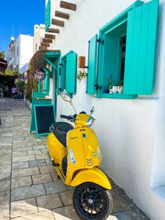 a yellow scooter parked in front of a white building with blue shutters