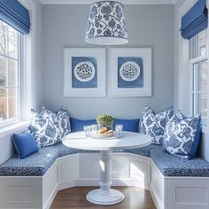 a white table with blue pillows on it in front of two framed pictures and windows