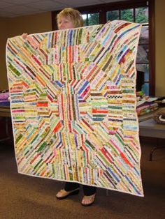 a woman holding up a large quilt made from strips of colored paper and threads