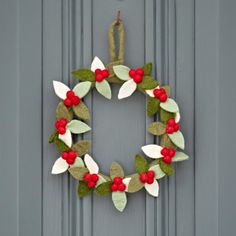 a wreath made out of felt with red berries and green leaves hanging on a gray door