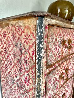 an old painted dresser with a green vase sitting on top of it next to a white wall