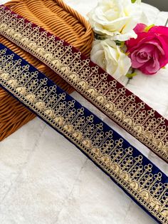 two pieces of blue and gold ribbon sitting next to each other on a table with flowers in the background