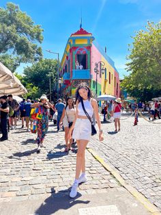 a woman walking down the street in front of a colorful building with people standing around