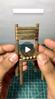 two hands holding a miniature wooden chair made out of wood planks and logs with the video below it