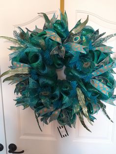 a green wreath with blue feathers on the front door is hanging on a white door