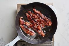 bacon is cooking in a frying pan on top of a stovetop burner