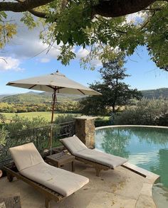 two chaise lounge chairs under an umbrella next to a swimming pool with a view