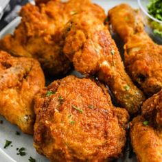 some fried food on a white plate with broccoli and dipping sauce in the background