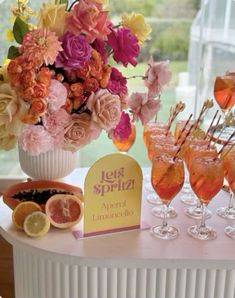 there are many glasses on the table with flowers and fruit in them, including grapefruits