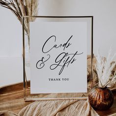 a card and gift sign sitting on top of a table next to some dried plants