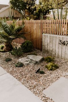 a small garden with rocks and plants in front of a wooden fenced yard area