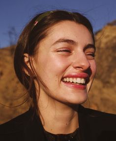 a woman smiling with her eyes closed in front of a mountain and blue sky behind her