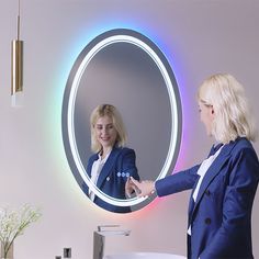 a woman in a blue suit is looking at her reflection in the mirror while standing next to a sink