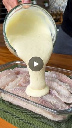 someone pouring sauce on raw fish in a glass dish