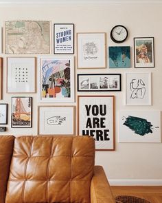 a brown leather couch sitting in front of a wall covered with pictures and framed art