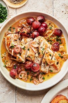 a white plate topped with fish covered in sauce and cherries next to other dishes