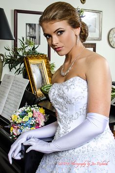 a woman in a wedding dress is holding a bouquet and looking at the camera while standing next to a piano