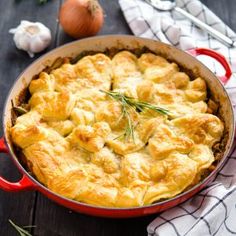 a casserole with meat and cheese in a red pan on a table next to garlic