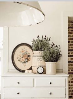 a white dresser topped with lots of flowers and plants next to a clock on top of it