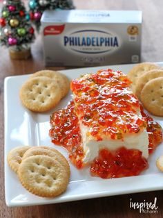 a white plate topped with crackers and cheese covered in sauce next to a box of philadelphia cheese